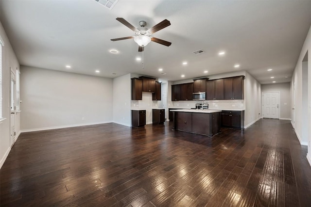120 Flexus Ln, Liberty Hill, TX 78642 - kitchen with stainless steel microwave, dark brown cabinetry, a kitchen island with sink, light countertops, and baseboards