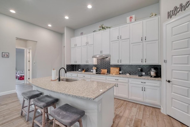 441 Double Eagle Ranch Dr, Cedar Creek, TX 78612 - kitchen with a sink, under cabinet range hood, decorative backsplash, a kitchen breakfast bar, and light wood-style flooring