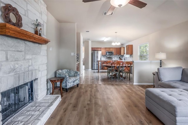 217 Baldwin St, Hutto, TX 78634 - living room featuring light wood finished floors, a ceiling fan, a chandelier, a fireplace with raised hearth, and baseboards