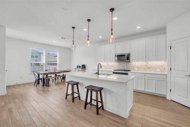 240 Harbors Ln, Leander, TX 78641 - kitchen featuring stainless steel microwave, a sink, range, light wood-type flooring, and decorative backsplash