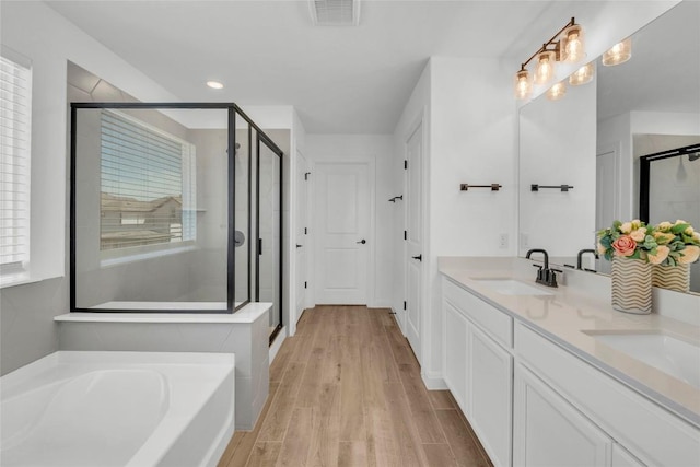 240 Harbors Ln, Leander, TX 78641 - bathroom with a stall shower, a garden tub, double vanity, wood finished floors, and recessed lighting