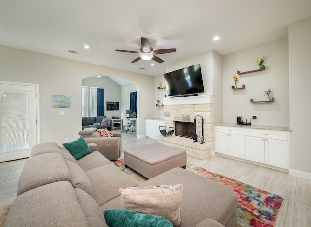 128 Naalehu Ct, Bastrop, TX 78602 - living area with arched walkways, ceiling fan, light wood-type flooring, a stone fireplace, and recessed lighting
