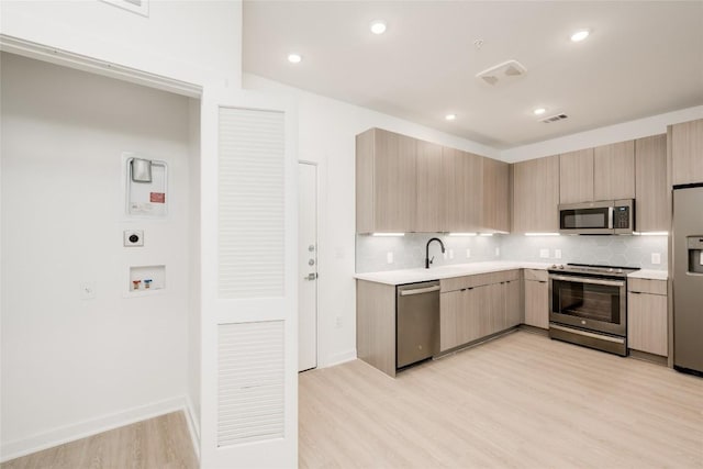 4802 S Congress Ave Unit 121, Austin, TX 78745 - kitchen with appliances with stainless steel finishes, light brown cabinetry, light countertops, light wood-style flooring, and tasteful backsplash