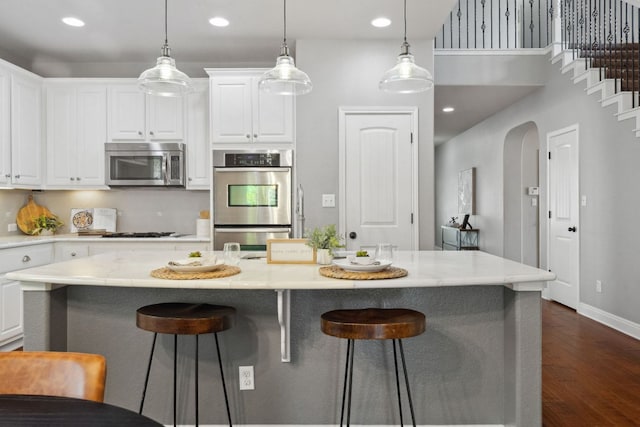 7820 Oteka Cv, Austin, TX 78735 - kitchen with appliances with stainless steel finishes, dark wood-style floors, white cabinetry, a breakfast bar, and a kitchen island with sink