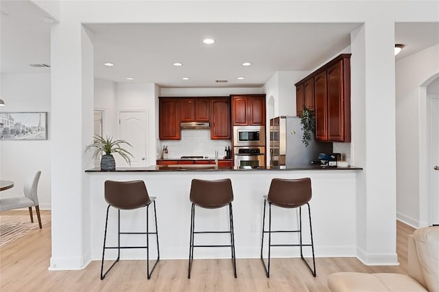 30 Stone Terrace Dr, Austin, TX 78734 - kitchen featuring appliances with stainless steel finishes, a peninsula, under cabinet range hood, decorative backsplash, and light wood finished floors