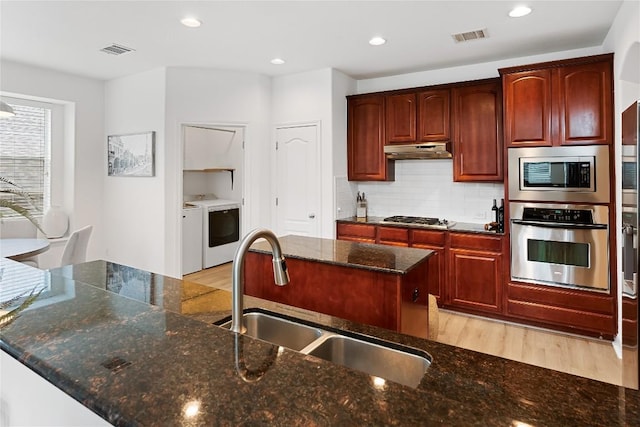 30 Stone Terrace Dr, Austin, TX 78734 - kitchen with washer and dryer, stainless steel appliances, under cabinet range hood, light wood finished floors, and backsplash
