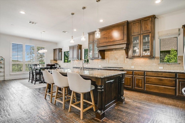 1016 Santaluz Path, Austin, TX 78732 - kitchen with a center island with sink, tasteful backsplash, glass insert cabinets, a breakfast bar area, and light stone counters