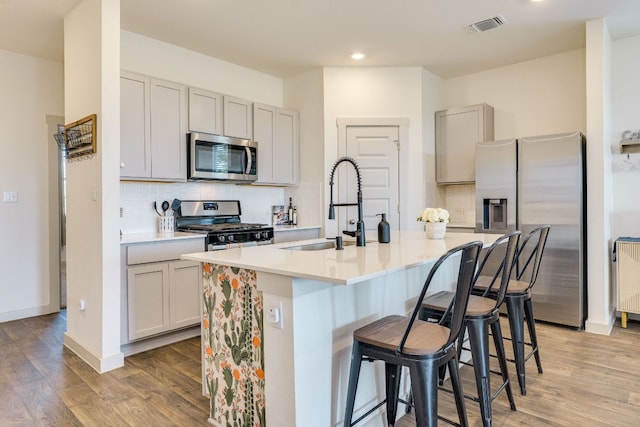 98 Barton Creek Ln, Hutto, TX 78634 - kitchen with appliances with stainless steel finishes, a sink, tasteful backsplash, a breakfast bar area, and light wood-style flooring