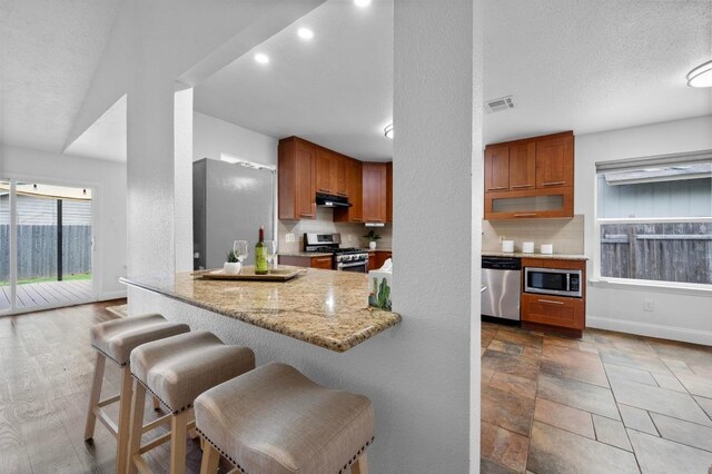 2405 Monarch Dr, Austin, TX 78748 - kitchen featuring appliances with stainless steel finishes, baseboards, under cabinet range hood, a breakfast bar, and light stone counters