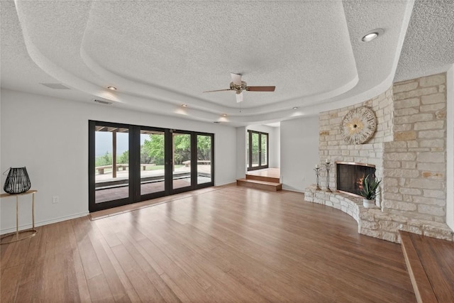 11105 Highview Dr, Belton, TX 76513 - unfurnished living room with a textured ceiling, a tray ceiling, a ceiling fan, a large fireplace, and wood finished floors
