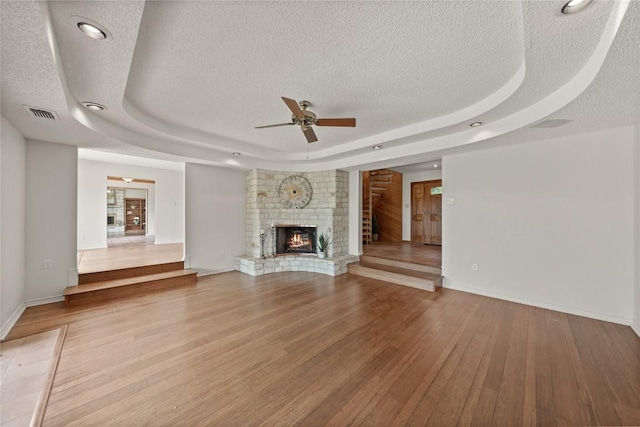 11105 Highview Dr, Belton, TX 76513 - unfurnished living room featuring a tray ceiling, a textured ceiling, a ceiling fan, wood finished floors, and a fireplace