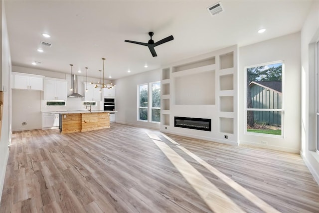 121 Mokolii Ct, Bastrop, TX 78602 - unfurnished living room featuring a ceiling fan, light wood-style flooring, recessed lighting, a chandelier, and a glass covered fireplace