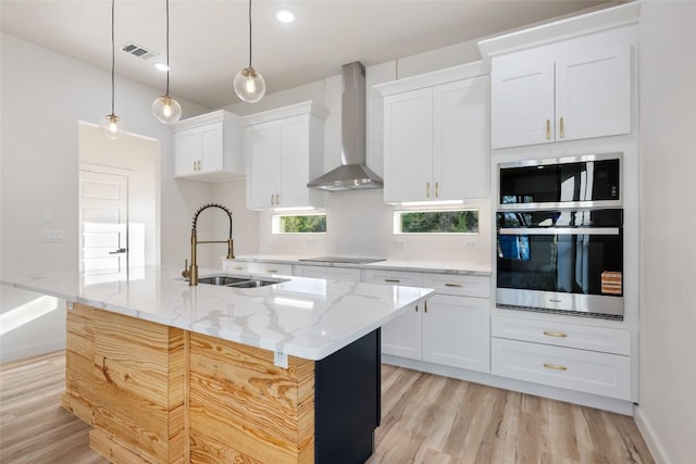 121 Mokolii Ct, Bastrop, TX 78602 - kitchen featuring wall chimney exhaust hood, a sink, light wood-type flooring, white cabinetry, and an island with sink