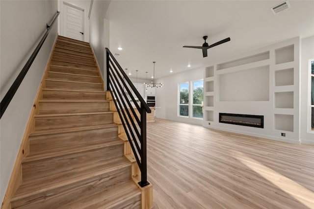 121 Mokolii Ct, Bastrop, TX 78602 - stairs featuring a ceiling fan, a glass covered fireplace, wood finished floors, a chandelier, and recessed lighting