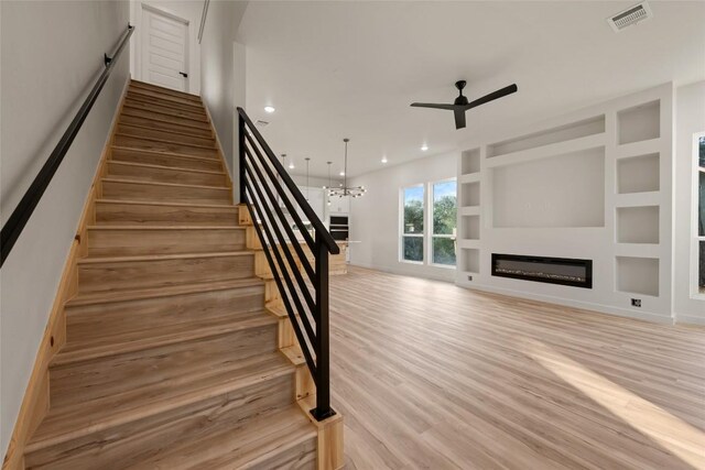 121 Mokolii Ct, Bastrop, TX 78602 - staircase featuring a ceiling fan, a glass covered fireplace, wood finished floors, a chandelier, and recessed lighting