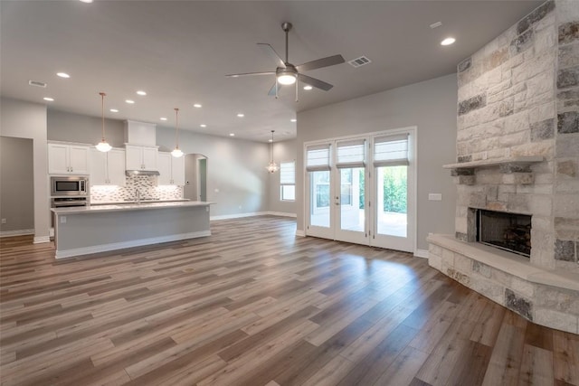 503 Fire Dance, Horseshoe Bay, TX 78657 - unfurnished living room with a stone fireplace, baseboards, wood finished floors, a ceiling fan, and recessed lighting