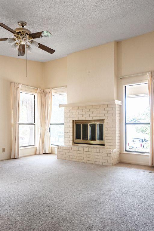 428 Summit Cir, Fredericksburg, TX 78624 - unfurnished living room with carpet flooring, a textured ceiling, a ceiling fan, and a brick fireplace