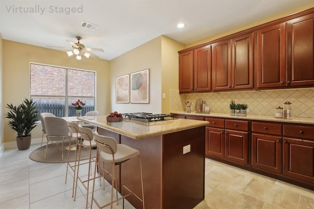 12109 Bryony Dr, Austin, TX 78739 - kitchen featuring tasteful backsplash, stainless steel gas stovetop, a kitchen bar, light stone counters, and a kitchen island