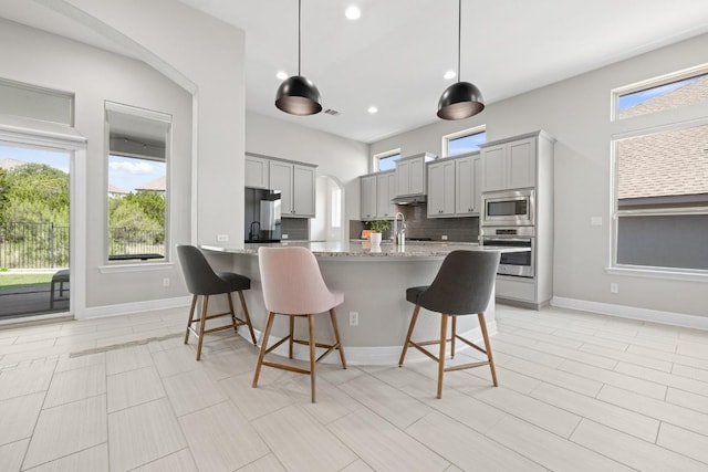 108 Panzano Dr, Georgetown, TX 78628 - kitchen featuring appliances with stainless steel finishes, gray cabinets, a breakfast bar, light stone countertops, and decorative backsplash