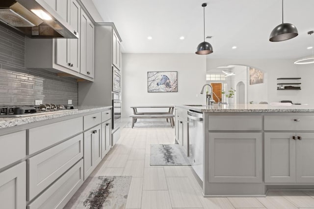 108 Panzano Dr, Georgetown, TX 78628 - kitchen featuring exhaust hood, stainless steel appliances, tasteful backsplash, arched walkways, and gray cabinets