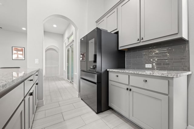 108 Panzano Dr, Georgetown, TX 78628 - kitchen with freestanding refrigerator, decorative backsplash, arched walkways, light stone counters, and gray cabinetry