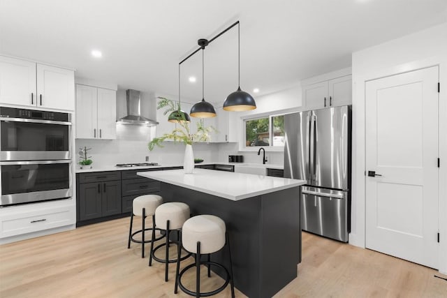 813 Cardiff Dr, Austin, TX 78745 - kitchen featuring wall chimney range hood, stainless steel appliances, a kitchen breakfast bar, light wood finished floors, and light countertops