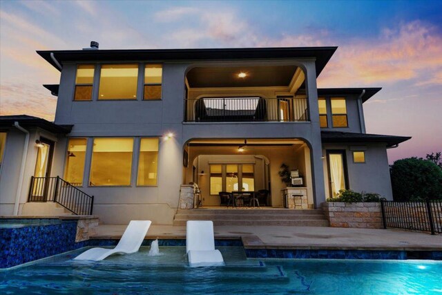 2037 Portobello Rd, Leander, TX 78641 - back of house at dusk featuring a balcony, a patio, an outdoor pool, and stucco siding
