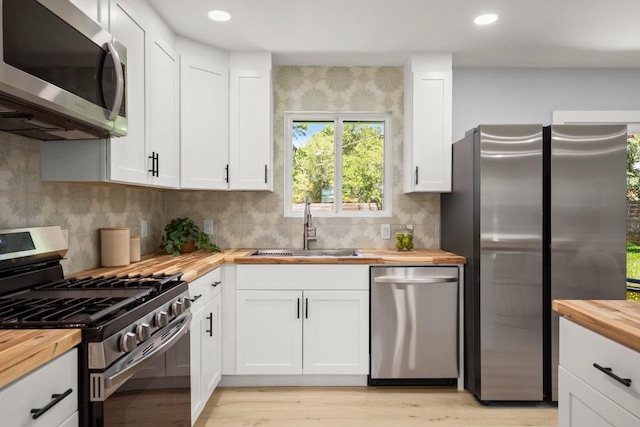 4802 Brighton Rd, Austin, TX 78745 - kitchen with butcher block counters, stainless steel appliances, white cabinets, backsplash, and light wood-type flooring