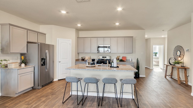 166 Caddo Bnd, Kyle, TX 78640 - kitchen featuring appliances with stainless steel finishes, gray cabinetry, dark wood-style floors, a kitchen breakfast bar, and recessed lighting
