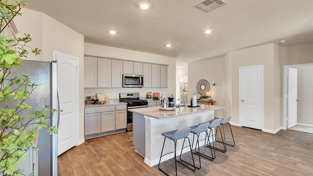 166 Caddo Bnd, Kyle, TX 78640 - kitchen featuring appliances with stainless steel finishes, light wood-style flooring, a kitchen bar, light stone counters, and recessed lighting