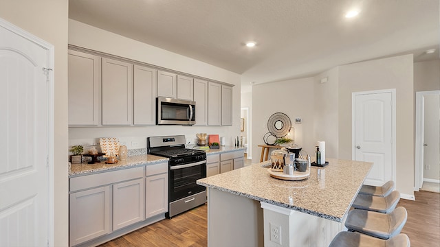 166 Caddo Bnd, Kyle, TX 78640 - kitchen featuring appliances with stainless steel finishes, gray cabinets, a kitchen island, a kitchen bar, and light wood-type flooring