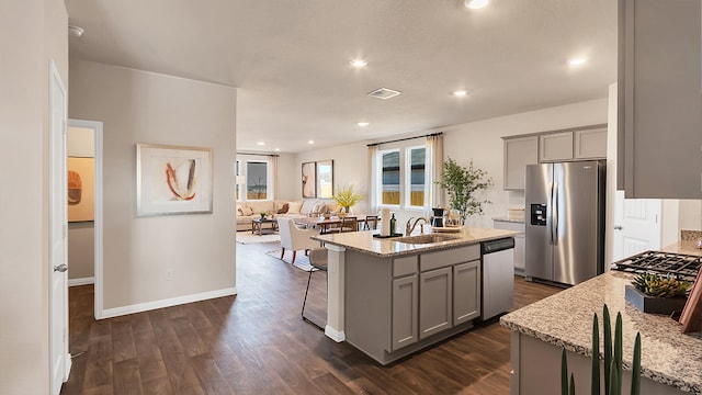 166 Caddo Bnd, Kyle, TX 78640 - kitchen with appliances with stainless steel finishes, gray cabinets, a center island with sink, dark wood-type flooring, and light stone countertops