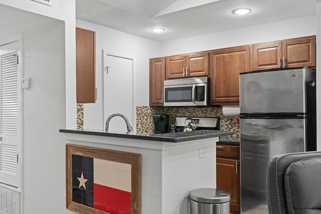 3601 Menchaca Rd Unit 215, Austin, TX 78704 - kitchen with stainless steel appliances, dark countertops, decorative backsplash, brown cabinets, and a peninsula