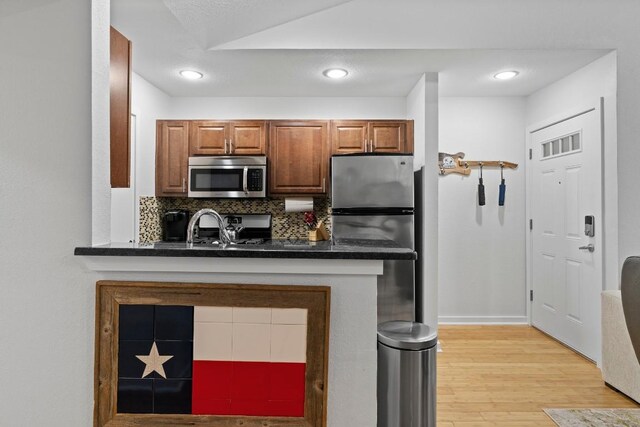 3601 Menchaca Rd Unit 215, Austin, TX 78704 - kitchen with stainless steel appliances, light wood-style flooring, dark countertops, brown cabinets, and backsplash