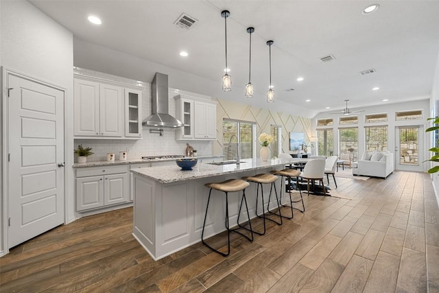 400 Saturnia Dr, Georgetown, TX 78613 - kitchen featuring wall chimney range hood, a sink, dark wood finished floors, tasteful backsplash, and an island with sink
