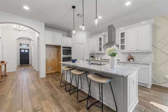 400 Saturnia Dr, Georgetown, TX 78613 - kitchen with wall chimney range hood, a sink, arched walkways, stainless steel appliances, and white cabinets
