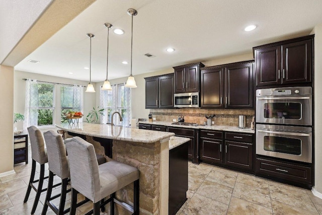 1312 Ravensbrook Bnd, Cedar Park, TX 78613 - kitchen with appliances with stainless steel finishes, tasteful backsplash, light stone countertops, a kitchen breakfast bar, and hanging light fixtures