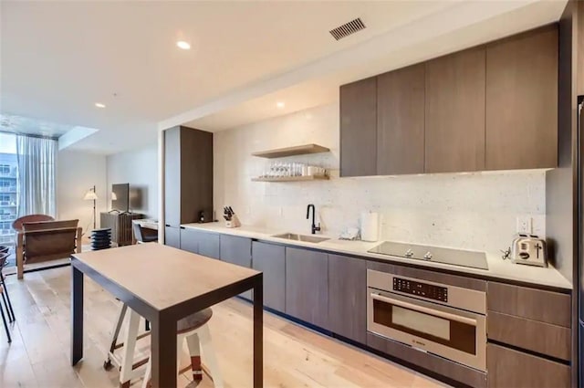 48 E Ave Unit 1210, Austin, TX 78701 - kitchen with oven, modern cabinets, black electric stovetop, backsplash, and light wood-style flooring