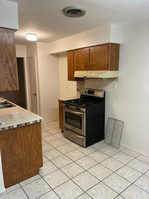 620 Amesbury Ln, Austin, TX 78752 - kitchen featuring gas stove, tile counters, light tile patterned floors, under cabinet range hood, and brown cabinets