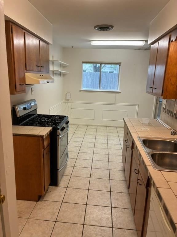 620 Amesbury Ln, Austin, TX 78752 - kitchen with tile countertops, stainless steel range with gas cooktop, under cabinet range hood, a sink, and light tile patterned floors