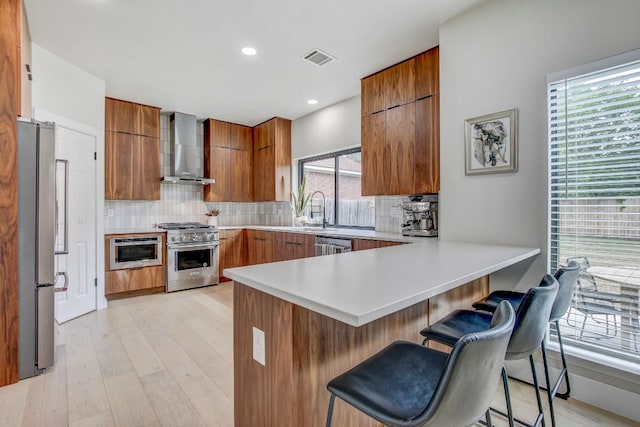 10840 Redmond Rd, Austin, TX 78739 - kitchen featuring wall chimney range hood, appliances with stainless steel finishes, brown cabinets, a peninsula, and decorative backsplash