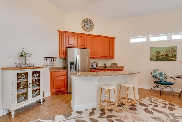 201 Thomas Ridge Rd, Burnet, TX 78611 - kitchen with stainless steel fridge, a kitchen breakfast bar, light tile patterned flooring, light stone counters, and brown cabinets