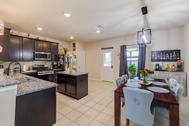 17020 Lathrop Ave, Pflugerville, TX 78660 - kitchen with appliances with stainless steel finishes, a center island, light tile patterned floors, dark brown cabinetry, and light stone counters
