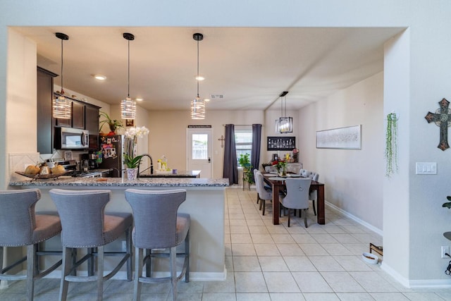 17020 Lathrop Ave, Pflugerville, TX 78660 - kitchen featuring stainless steel appliances, light stone counters, a peninsula, light tile patterned floors, and hanging light fixtures