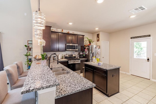 17020 Lathrop Ave, Pflugerville, TX 78660 - kitchen featuring appliances with stainless steel finishes, dark brown cabinets, a kitchen island, light stone countertops, and hanging light fixtures