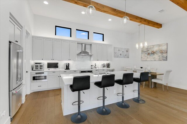 13322 Galleria Cir, Austin, TX 78738 - kitchen featuring high end refrigerator, wall chimney exhaust hood, light countertops, beam ceiling, and light wood-style flooring