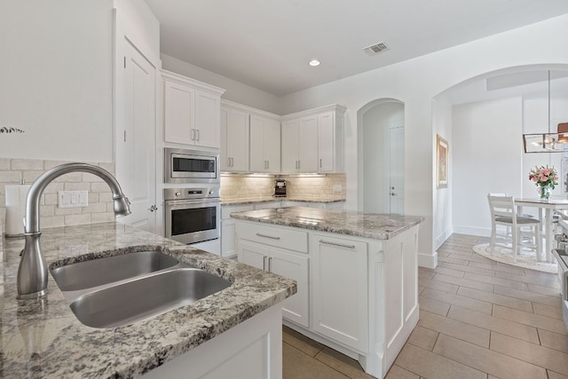 260 Unbridled, Austin, TX 78737 - kitchen with stainless steel appliances, a sink, white cabinets, backsplash, and arched walkways