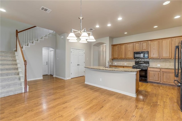 1911 Nelson Ranch Loop, Cedar Park, TX 78613 - kitchen featuring black appliances, arched walkways, tasteful backsplash, a center island with sink, and light wood finished floors