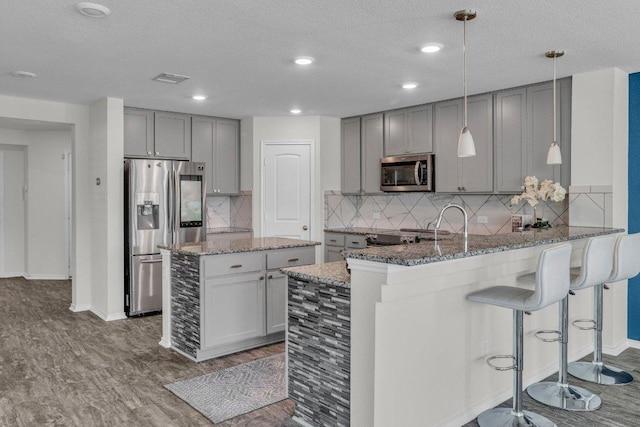 18909 James Carter Jr St, Manor, TX 78653 - kitchen with appliances with stainless steel finishes, gray cabinets, stone countertops, wood finished floors, and a kitchen island