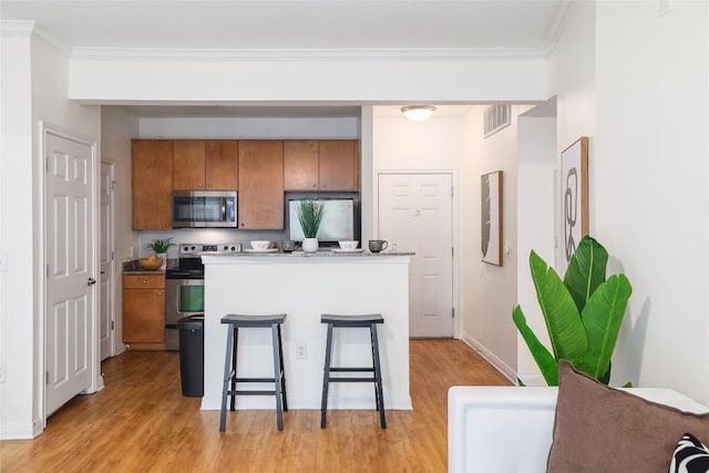 2502 Leon St Unit 208, Austin, TX 78705 - kitchen with stainless steel appliances, brown cabinets, crown molding, light wood-type flooring, and a breakfast bar area